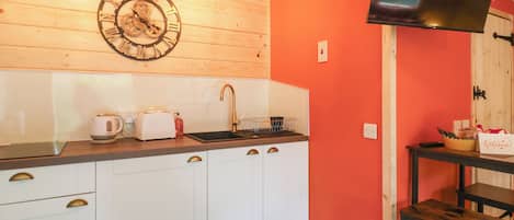 A kitchen with white cabinets, a black countertop, a clock, and a television mounted on the wall.