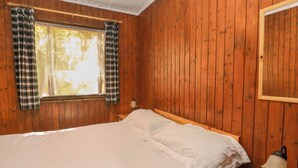 A wooden-paneled room with a bed, a window with plaid curtains, and a nightstand with a lamp. - Lodge 6 - "alder" (Isle of Arran)