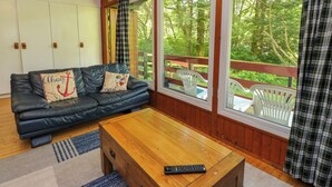 A cozy living room with a leather sofa, wooden coffee table, and large windows offering a view of the outdoors. - Lodge 6 - "alder" (Isle of Arran)