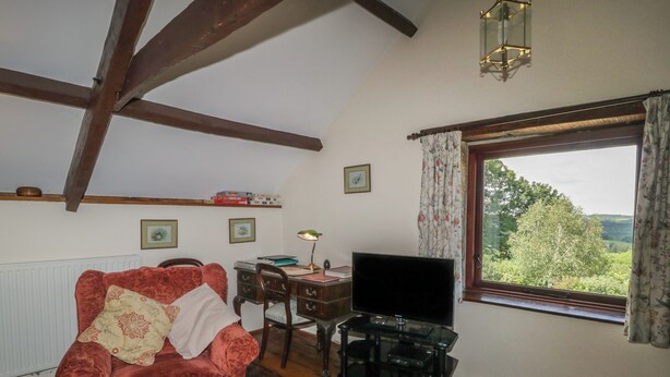 Una habitación acogedora con un sofá de terciopelo rojo, un escritorio de madera con una computadora, un televisor y una ventana con vistas a la vegetación.