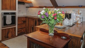 Una cocina con armarios de madera, horno empotrado, un florero con flores y una cafetera en la encimera.