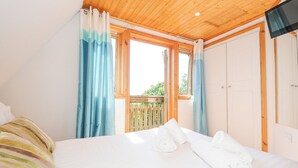 Een slaapkamer met een groot bed, houten plafond en uitzicht op een houten terras.