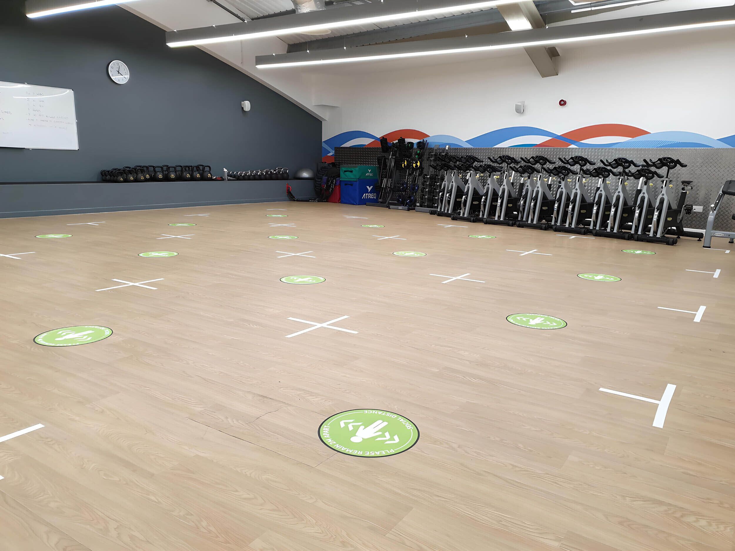 Un gimnasio con equipamiento de ejercicio, una pizarra y marcas en el suelo para indicar la dirección.