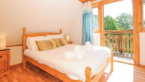 Een bed met houten frame, witte lakens, een nachtkastje met lamp en uitzicht op een houten terras door een glazen deur.