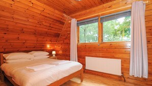 A wooden-paneled bedroom with a bed, a nightstand, a window with curtains, and a radiator. - Lodge 32 - Cowslip (Newton Abbot)