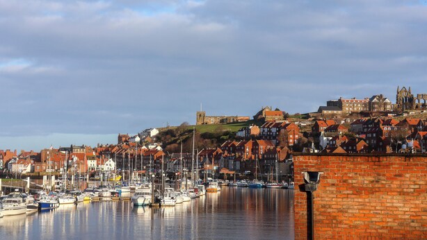 A harbor with boats, a brick wall, and buildings in the background.