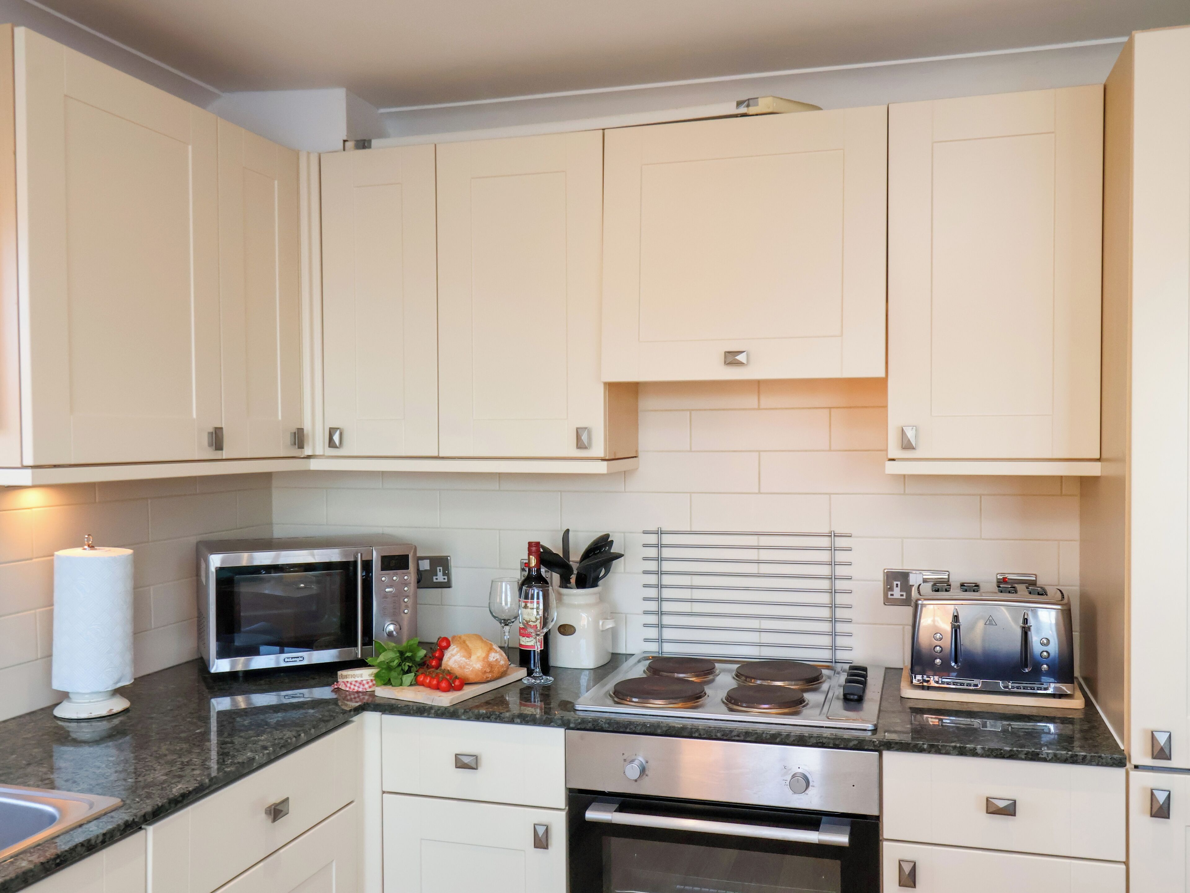 Una cocina con armarios blancos, un microondas de acero inoxidable, un tostador y una estufa.