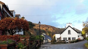 A narrow street with a white building with a gabled roof, a stone wall, and a tree with autumn leaves. - Old Farm Cottage (Ilfracombe)