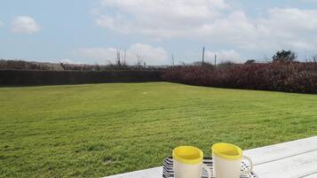 Un espacio al aire libre con césped, una mesa de picnic y dos tazas amarillas sobre una bandeja.