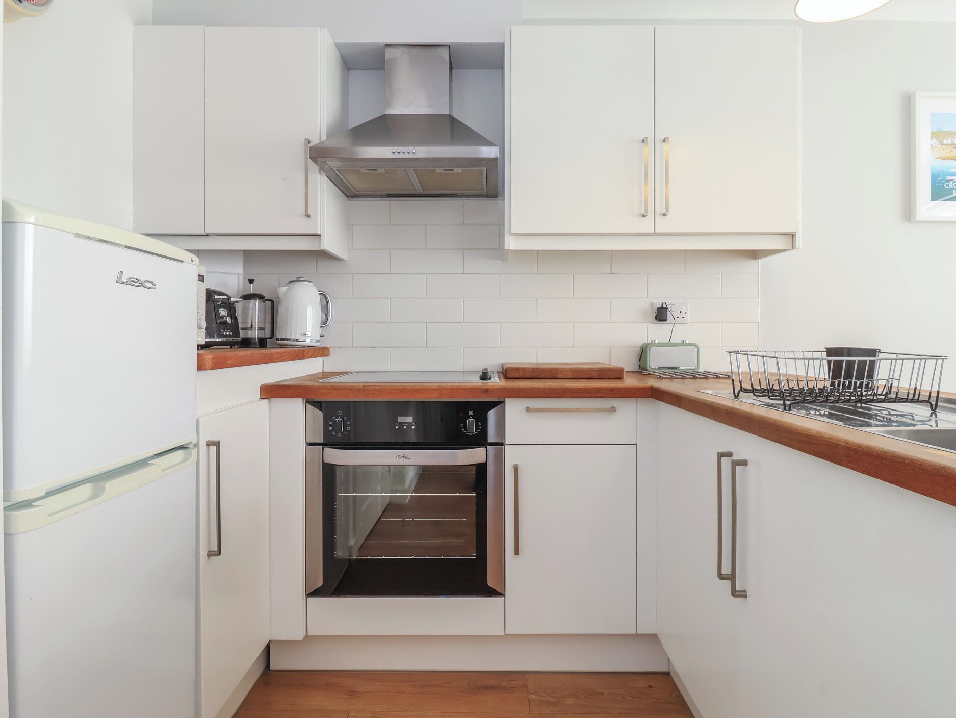 Een kleine keuken met witte kasten, een inbouwoven, een roestvrijstalen afzuigkap en een houten aanrecht.