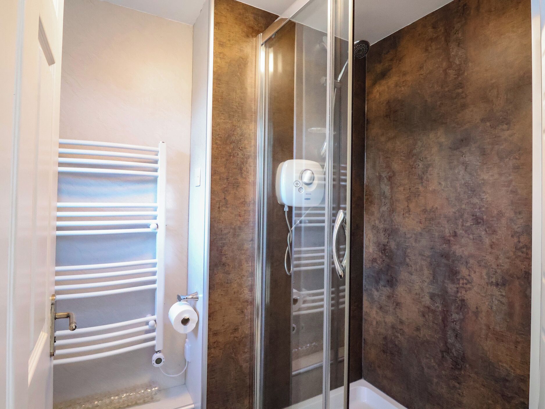 A modern bathroom with a glass shower enclosure, a white towel rack, and a toilet paper holder.