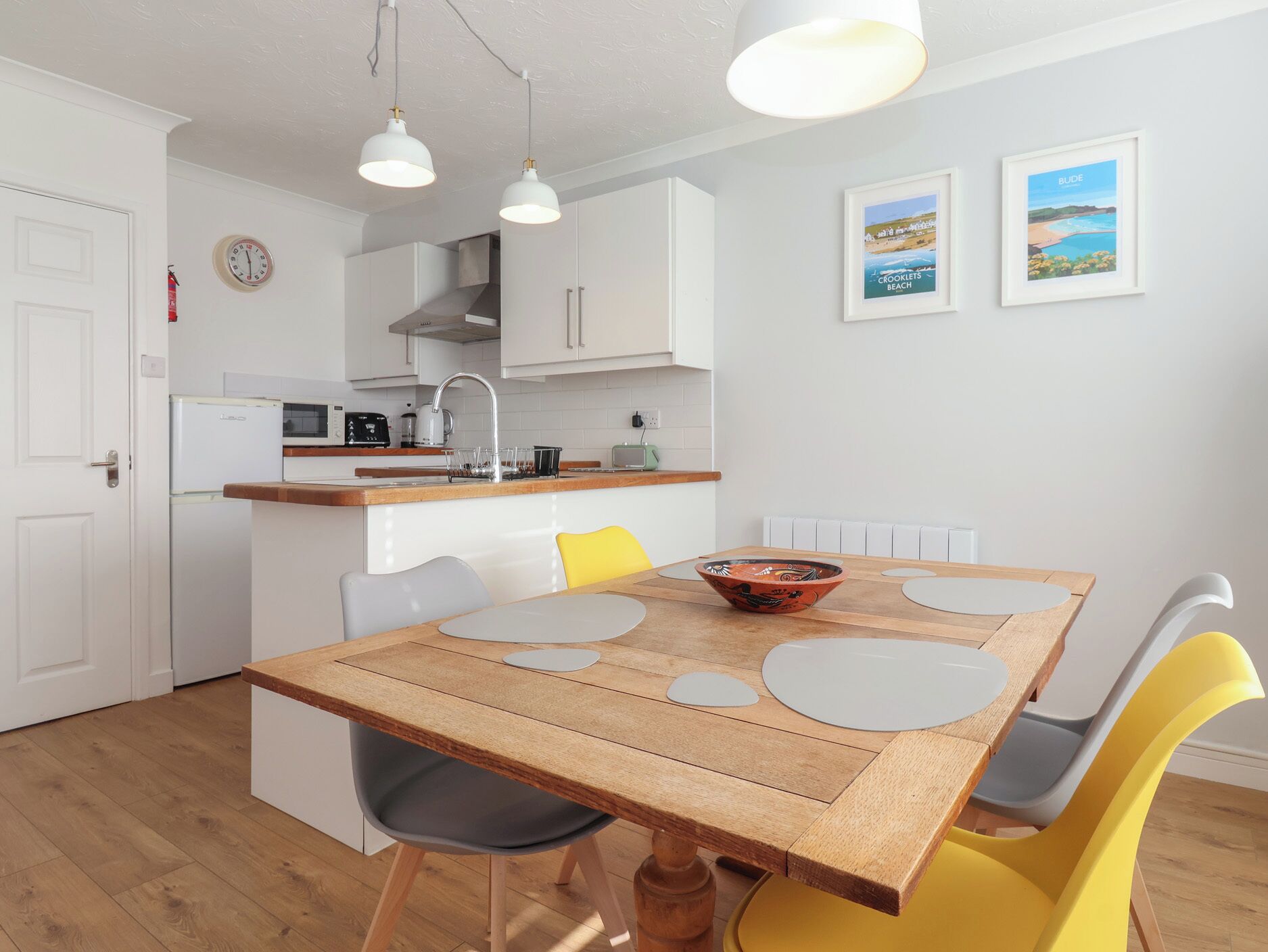 A compact kitchen with white cabinets, a wooden dining table with four chairs, and a small island with a sink.