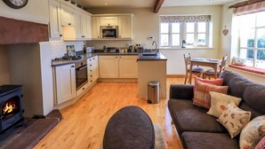 A modern kitchen with a central island, wooden flooring, and a cozy seating area with a sofa and cushions. - Squirrel Cottage (Keswick)