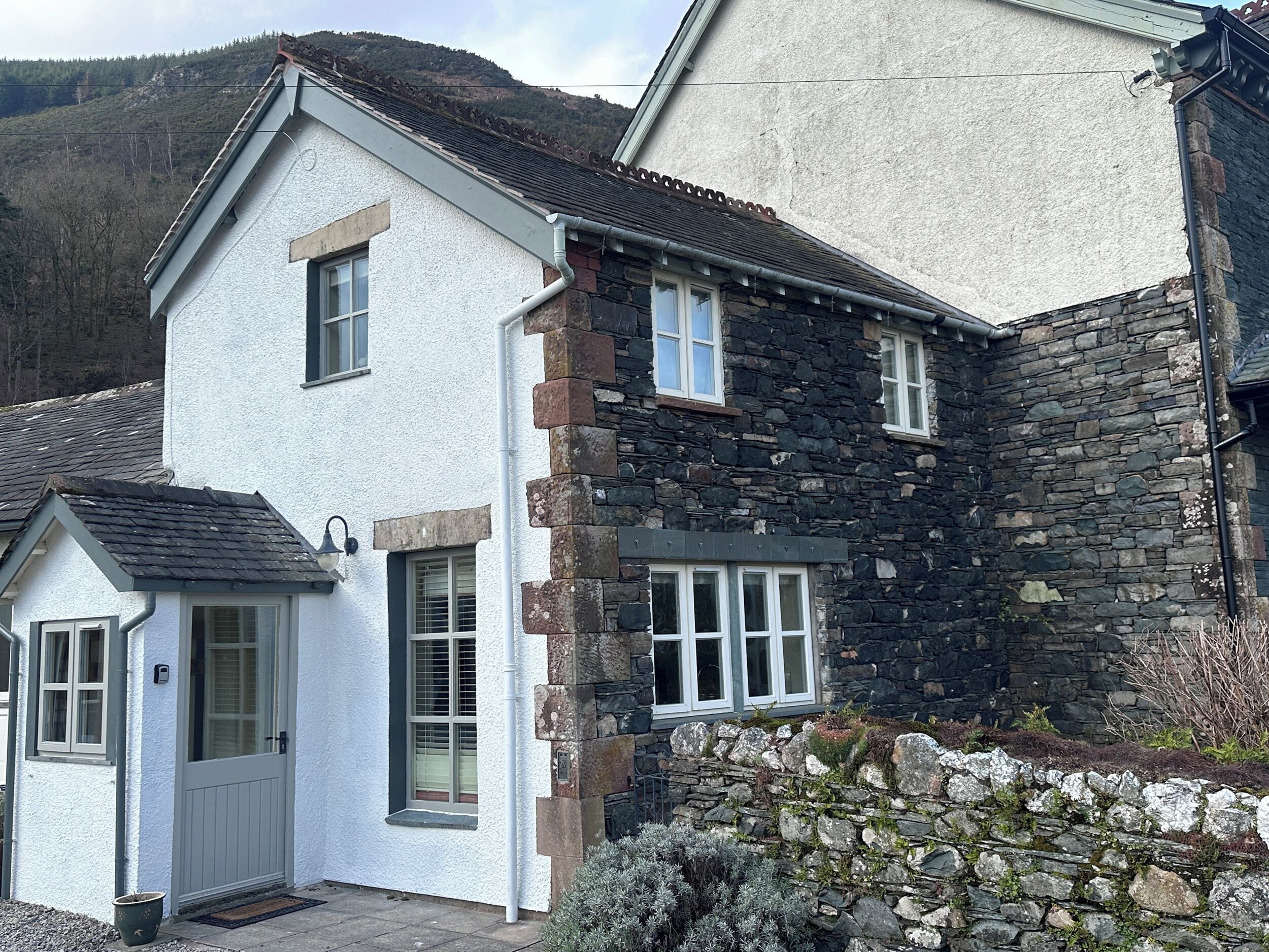 A two-story house with a white exterior and stone accents, featuring a small porch and a stone wall.