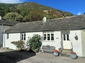 A white building with a grey roof, a bench, and flower pots in front. - Fox Howe (Keswick)