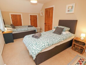 A bedroom with two beds, wooden doors, a small bedside table with a lamp, and a patterned rug.