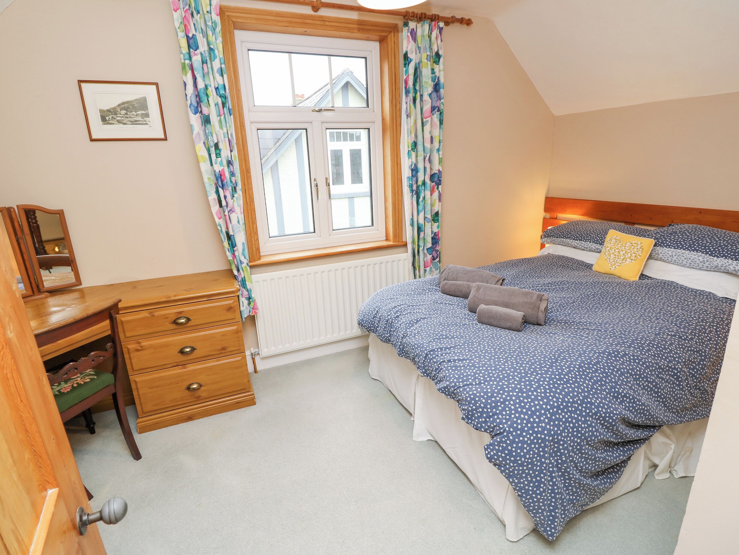 A bedroom with a bed, a dresser, a window with curtains, a radiator, and a picture on the wall.