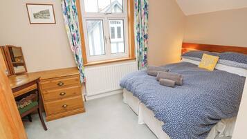 A bedroom with a bed, a dresser, a window with curtains, a radiator, and a picture on the wall.