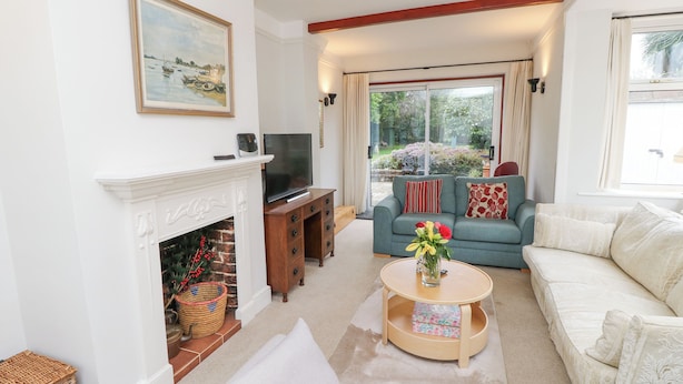 A living room with a fireplace, a television, a sofa, and a window with a view of greenery. - Framingham (Hayling Island)