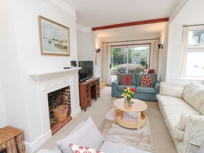 A living room with a fireplace, a television, a sofa, and a window with a view of greenery. - Framingham (Hayling Island)