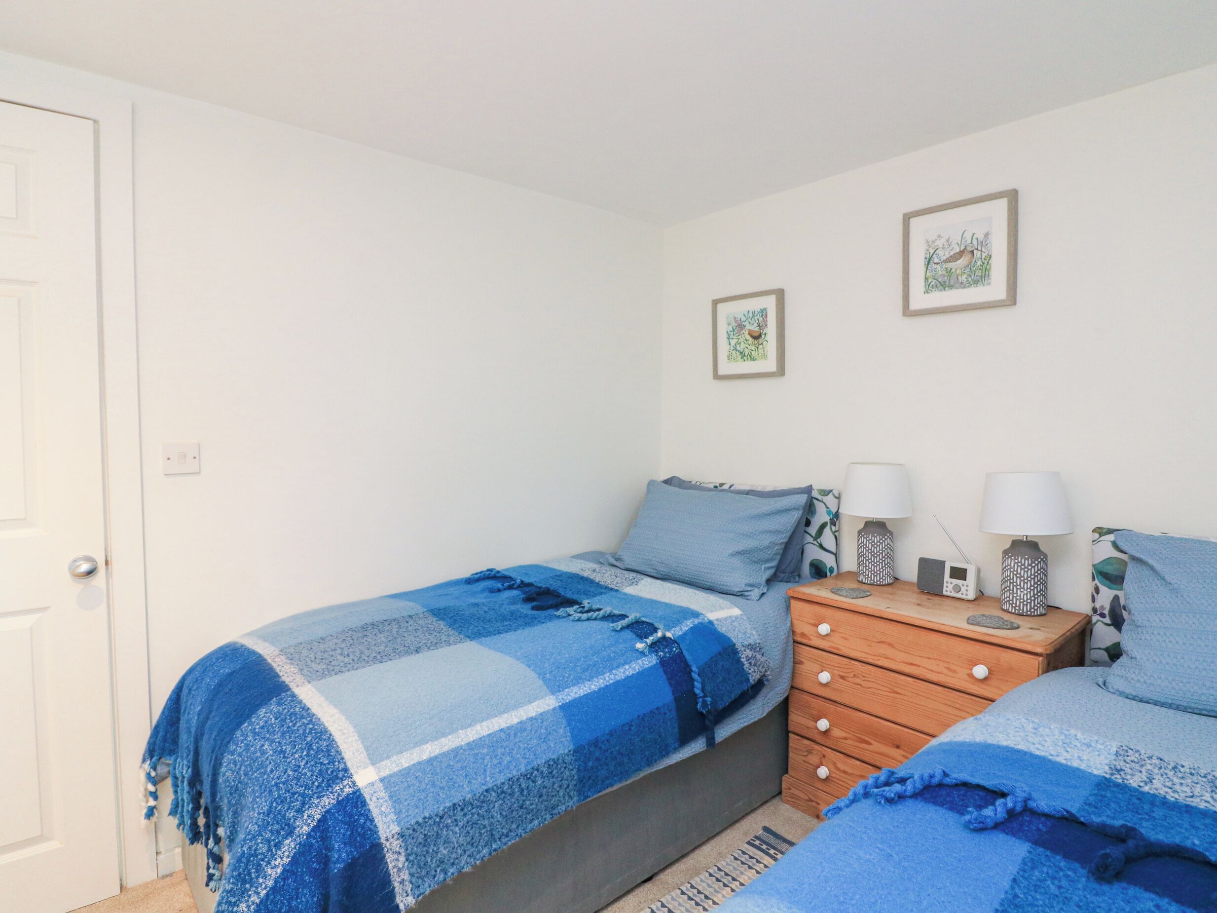 A bedroom with two beds, a wooden dresser, and two wall-mounted lamps.