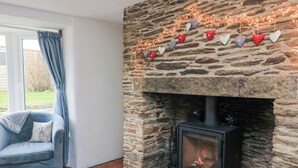 Une pièce chaleureuse avec une cheminée en pierre, un canapé bleu et une vue sur l’extérieur.