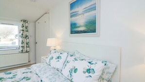 Une chambre à coucher avec un lit, une fenêtre avec des rideaux, une table de chevet avec une lampe et un tableau accroché au mur.