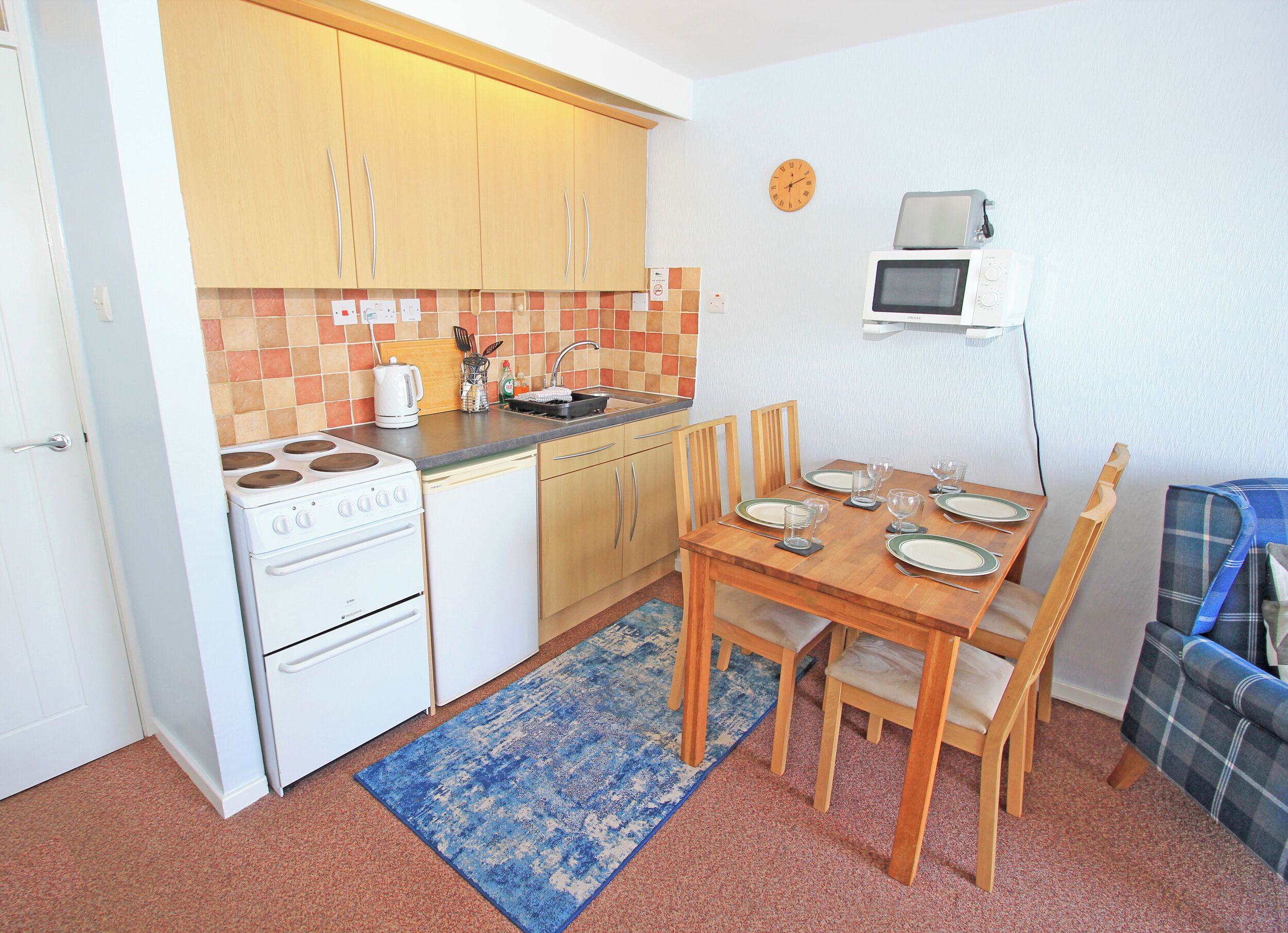 A compact kitchen with a stove, microwave, and a dining table set for four.