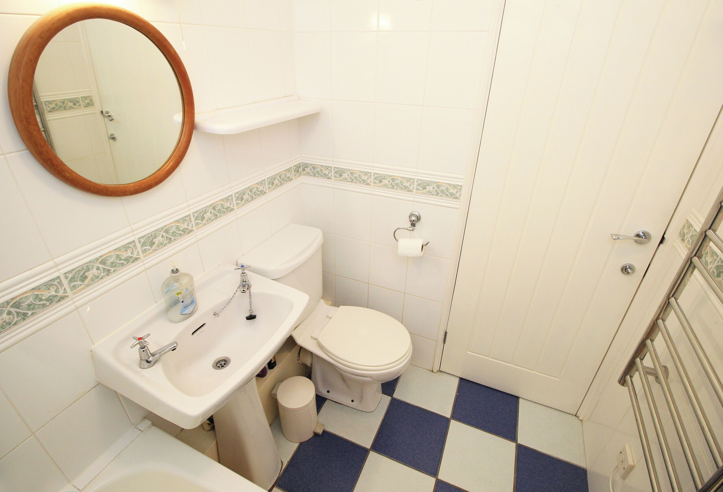 Ein Badezimmer mit weißem Waschbecken, Toilette und Badewanne, einem Spiegel und einem Schachbrettboden.