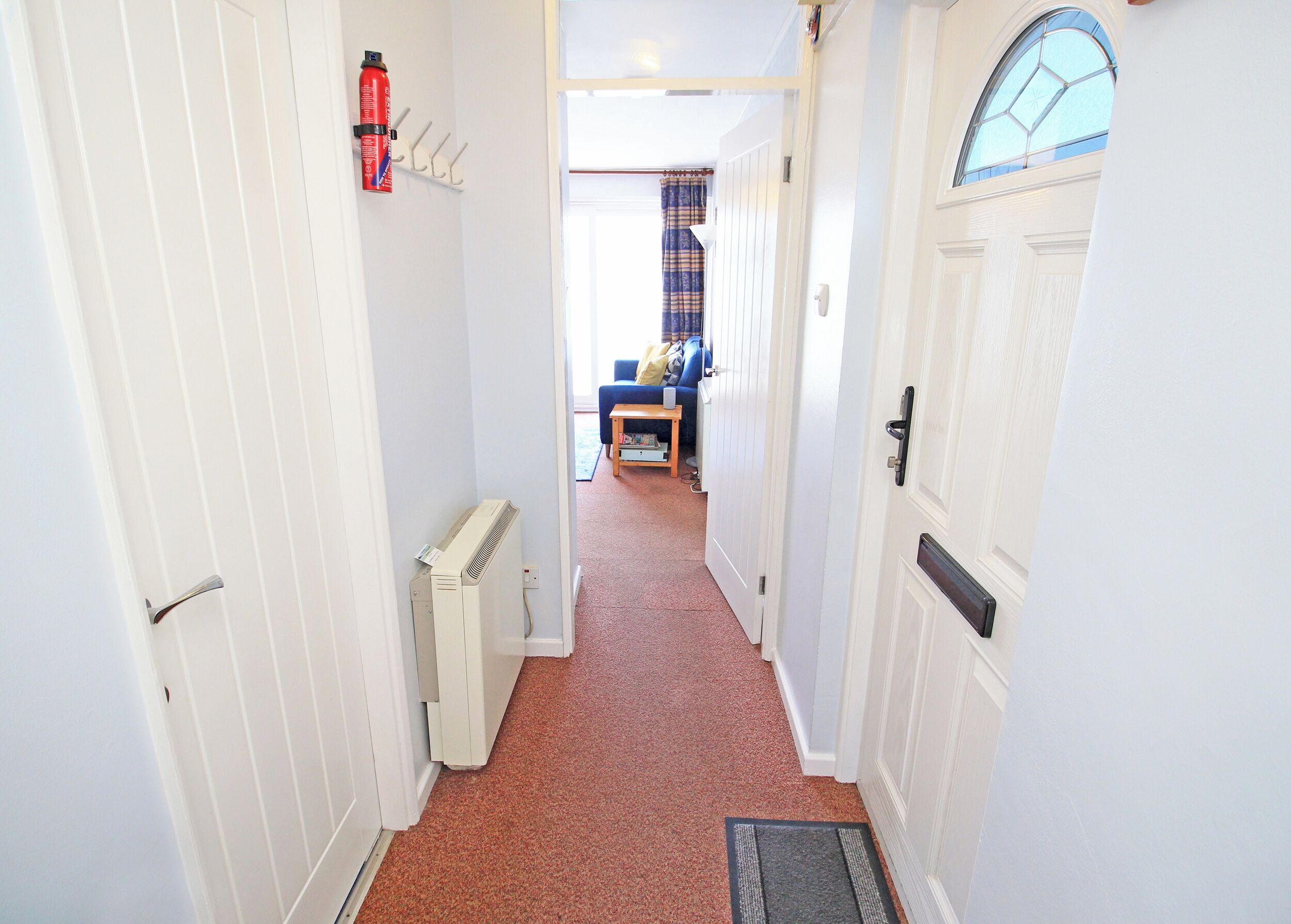A narrow hallway with a radiator, a fire extinguisher, and a door leading to a room with a window and a blue chair.