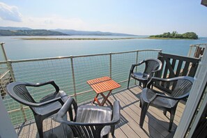 Eine Terrasse mit vier Stühlen und einem kleinen Tisch, mit Blick auf ruhiges Wasser und die Ferne.