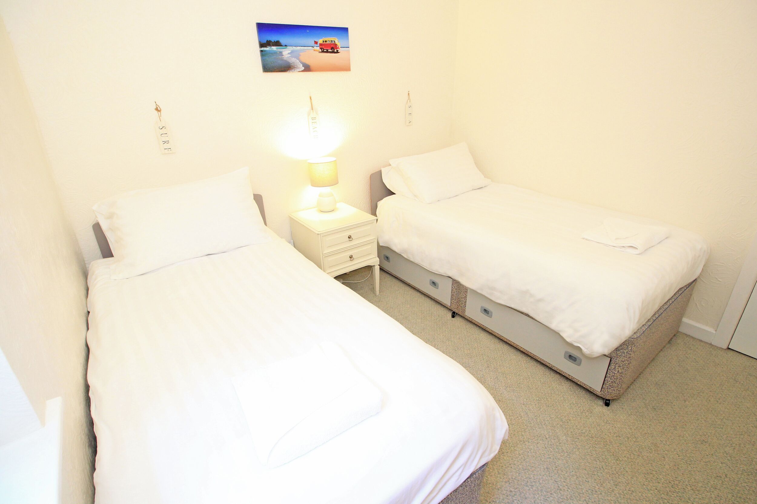 A twin room with two single beds, a bedside table with a lamp, and a small wall-mounted shelf.