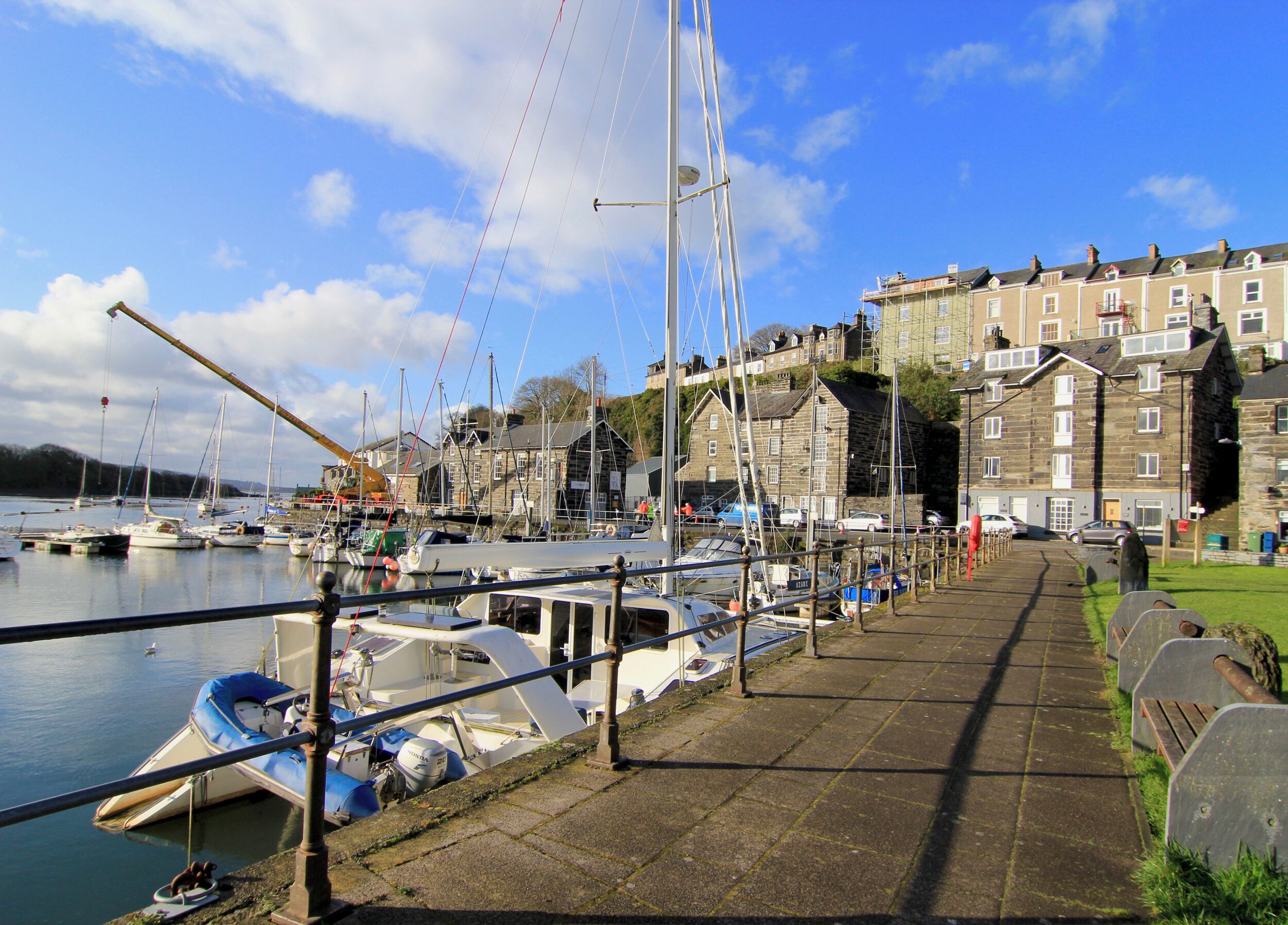 A harbor with boats docked along the waterfront, a stone building with multiple stories, and a clear sky.