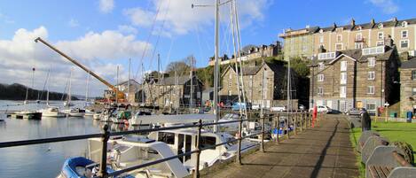 A harbor with boats docked along the waterfront, a stone building with multiple stories, and a clear sky.