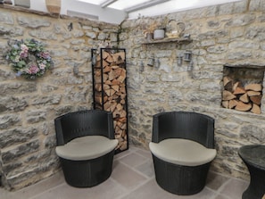 A stone-walled outdoor seating area with wicker chairs and a fire pit. - Rose Cottage (Buxton)