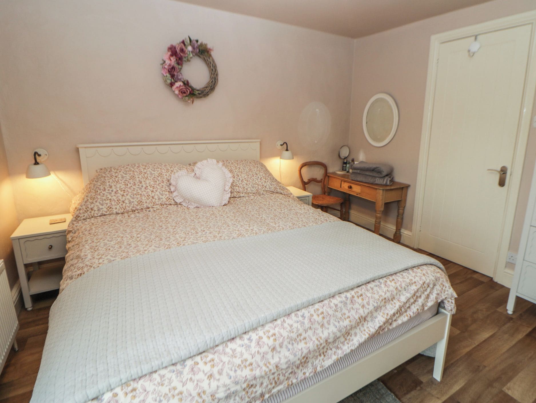 Un dormitorio con cama, mesita de noche, cómoda, espejo y puerta.