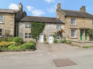 A stone building with a central entrance, a small garden with flowers, and a metal manhole cover in the foreground.