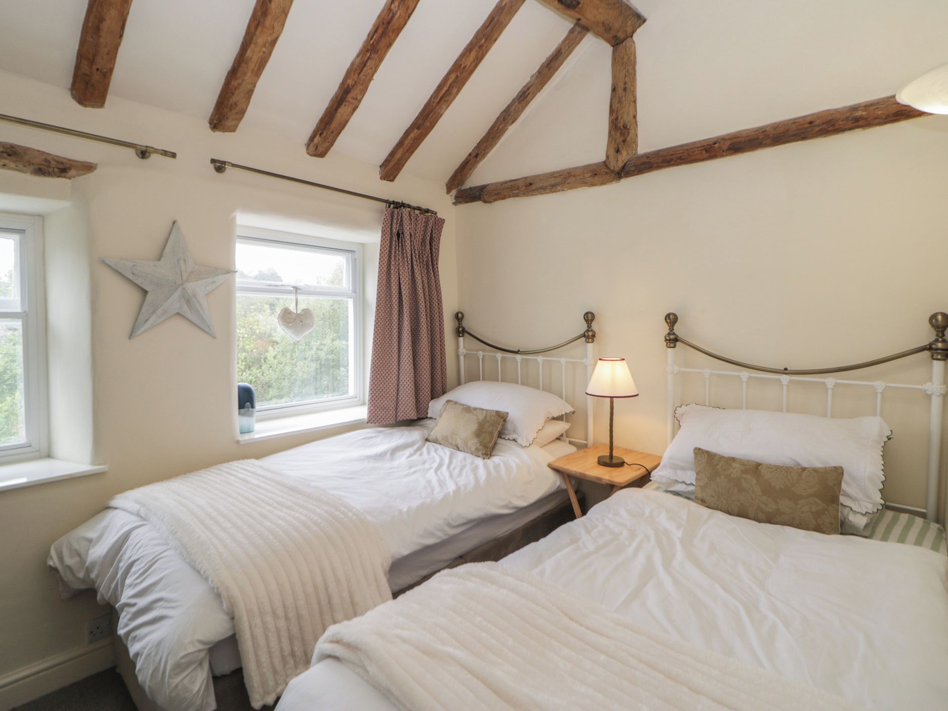 Un dormitorio con dos camas individuales, una ventana con cortinas, una decoración con estrellas y una lámpara de noche.