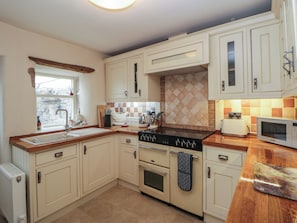 A kitchen with white cabinets, a stove, a microwave, and a window. - Rose Cottage (Buxton)