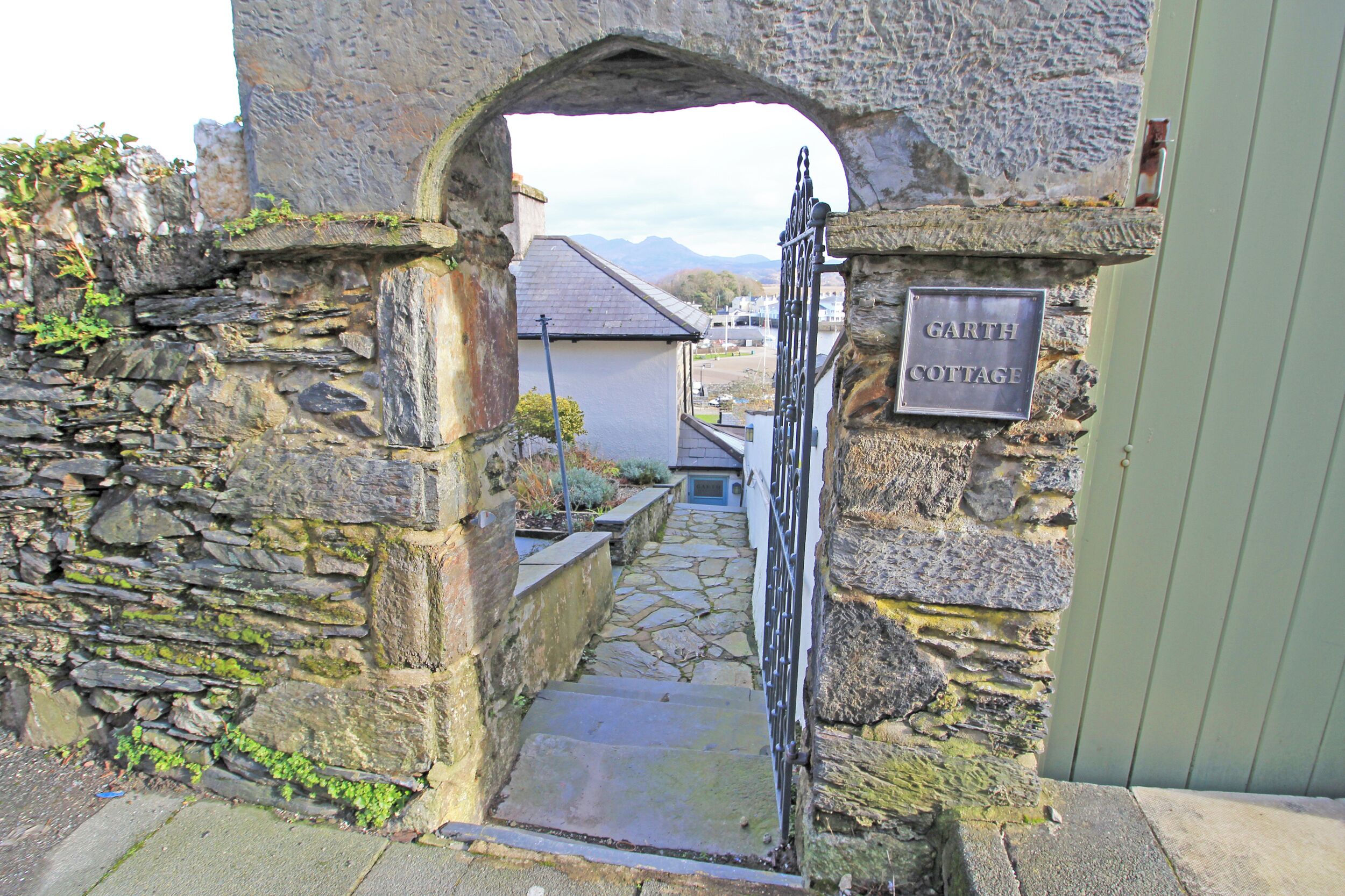 A stone archway leading to a cottage labeled 'Garth Cottage' with a stone pathway and a metal gate.