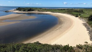 A coastal landscape with a sandy beach, calm water, and a distant view of the sea under a clear sky.