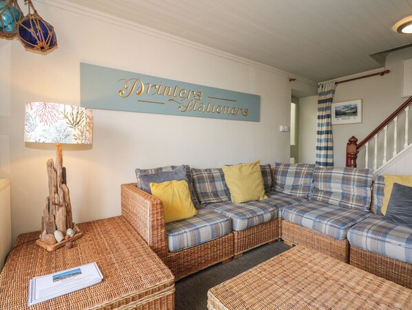 A living room with a wicker sofa, a lamp, and a sign that reads "Printers & Stationers". - Garth Cottage (Porthmadog)