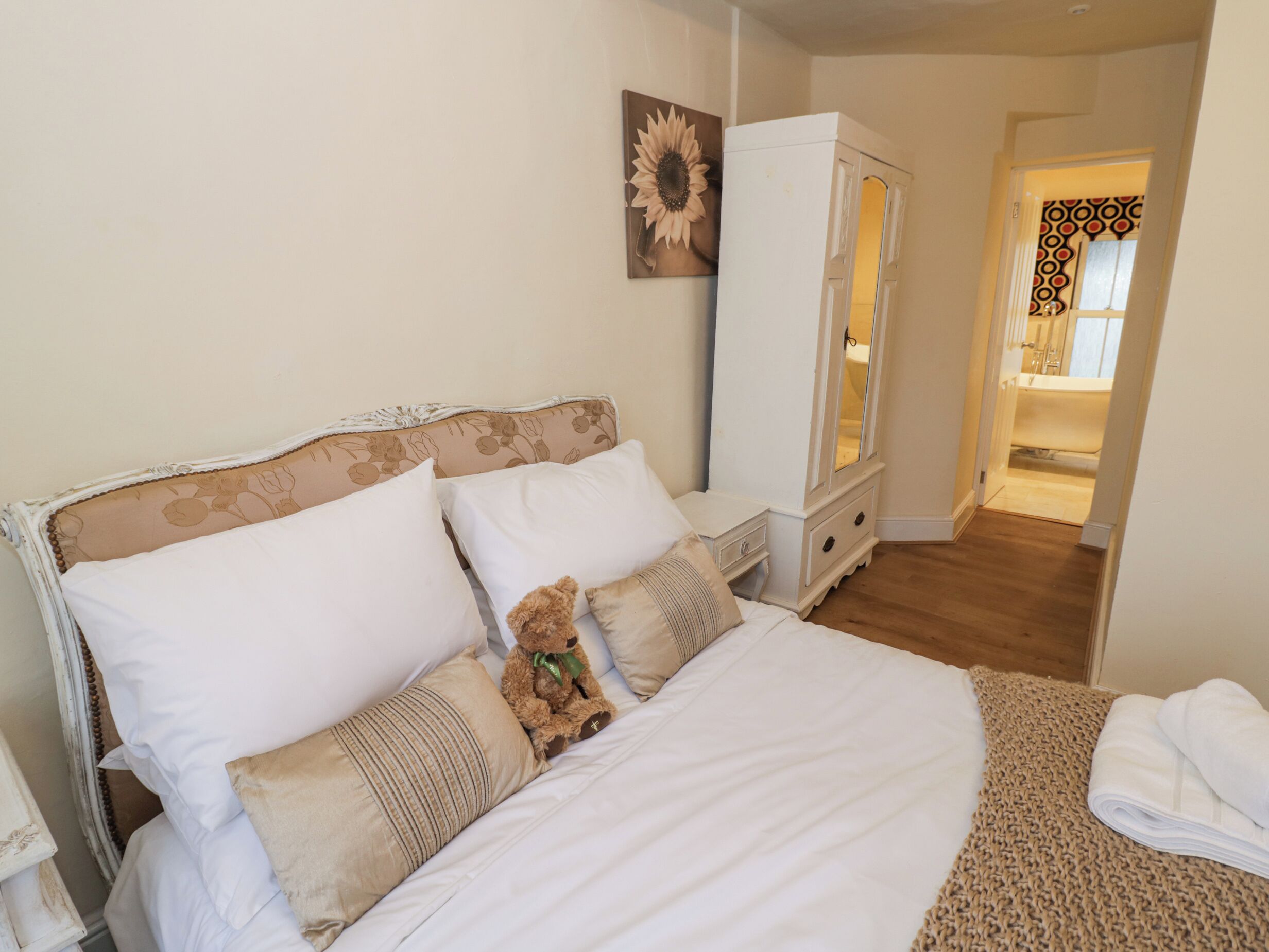 A bedroom with a bed, pillows, a teddy bear, a wardrobe, and a mirror.
