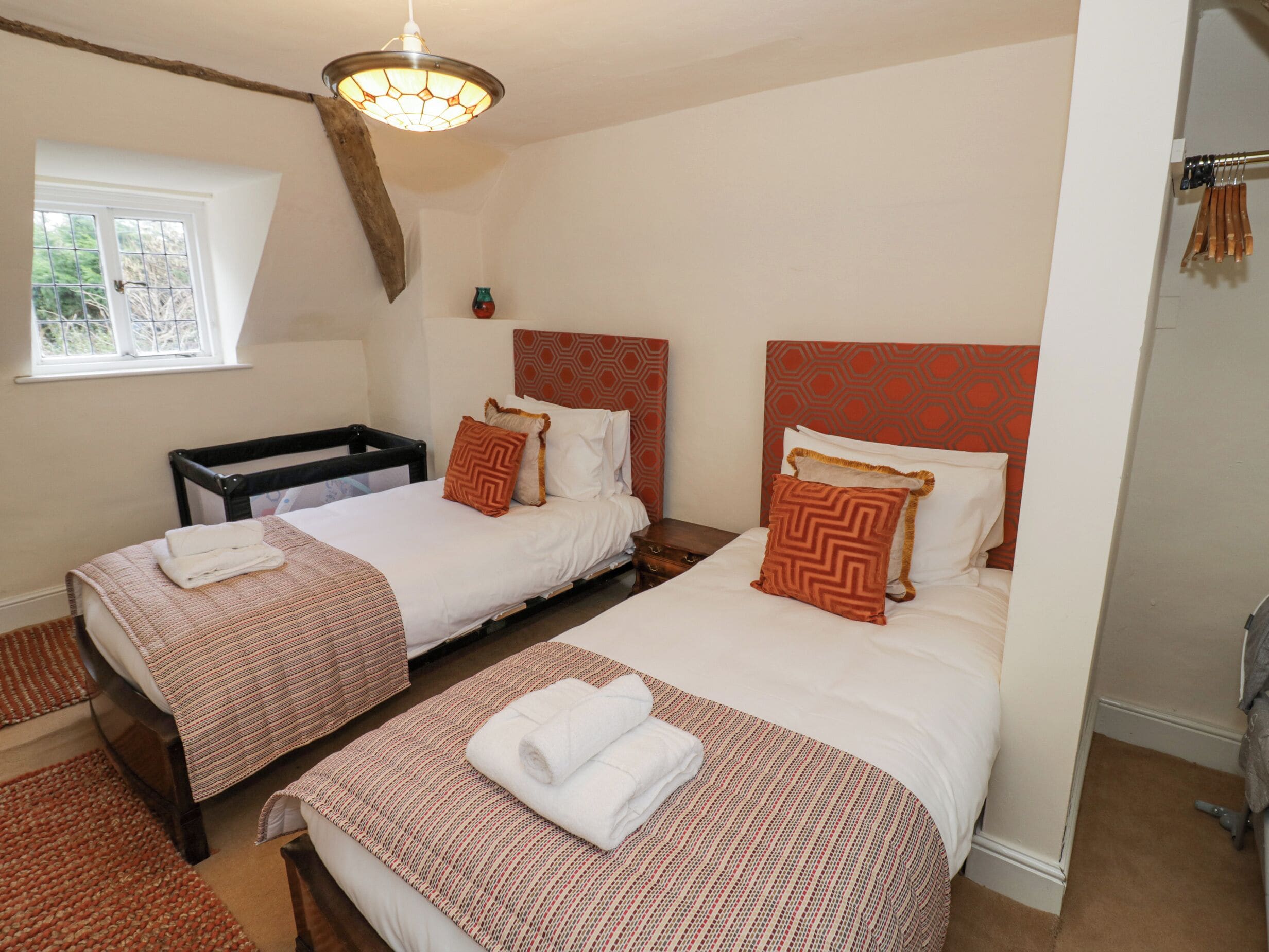 A hotel room with two beds, a window, and a hanging light fixture.