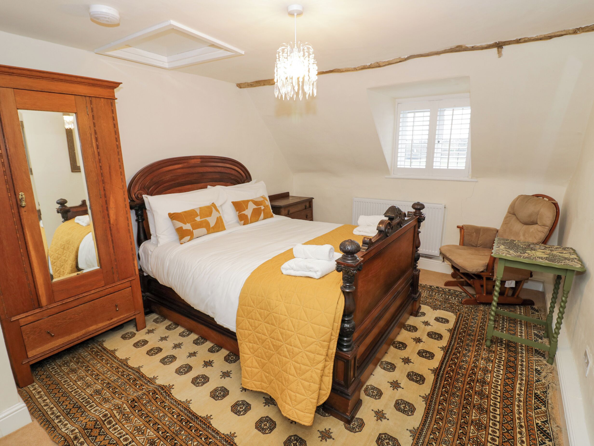 Une chambre à coucher avec un lit en bois, un miroir, une chaise verte et un tapis à motifs.