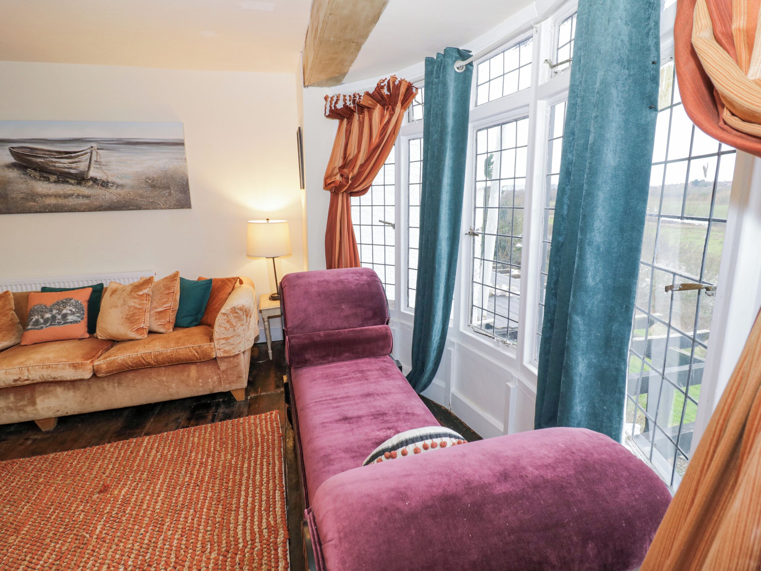 Una habitación acogedora con un sofá, un sillón morado, una alfombra, una lámpara y un cuadro de un barco en la pared.