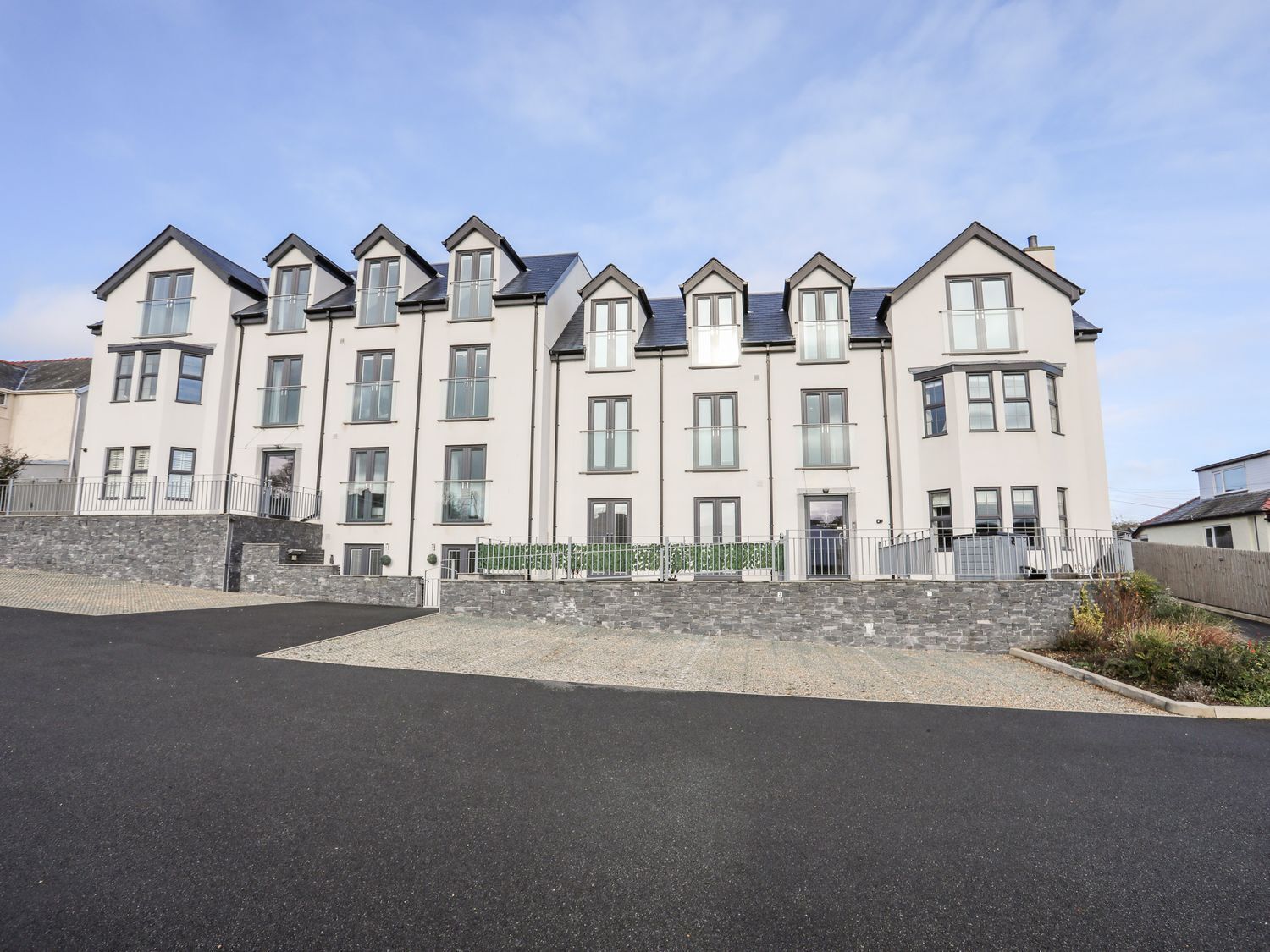 A multi-story residential building with a symmetrical facade, multiple windows, and a stone wall at the base.