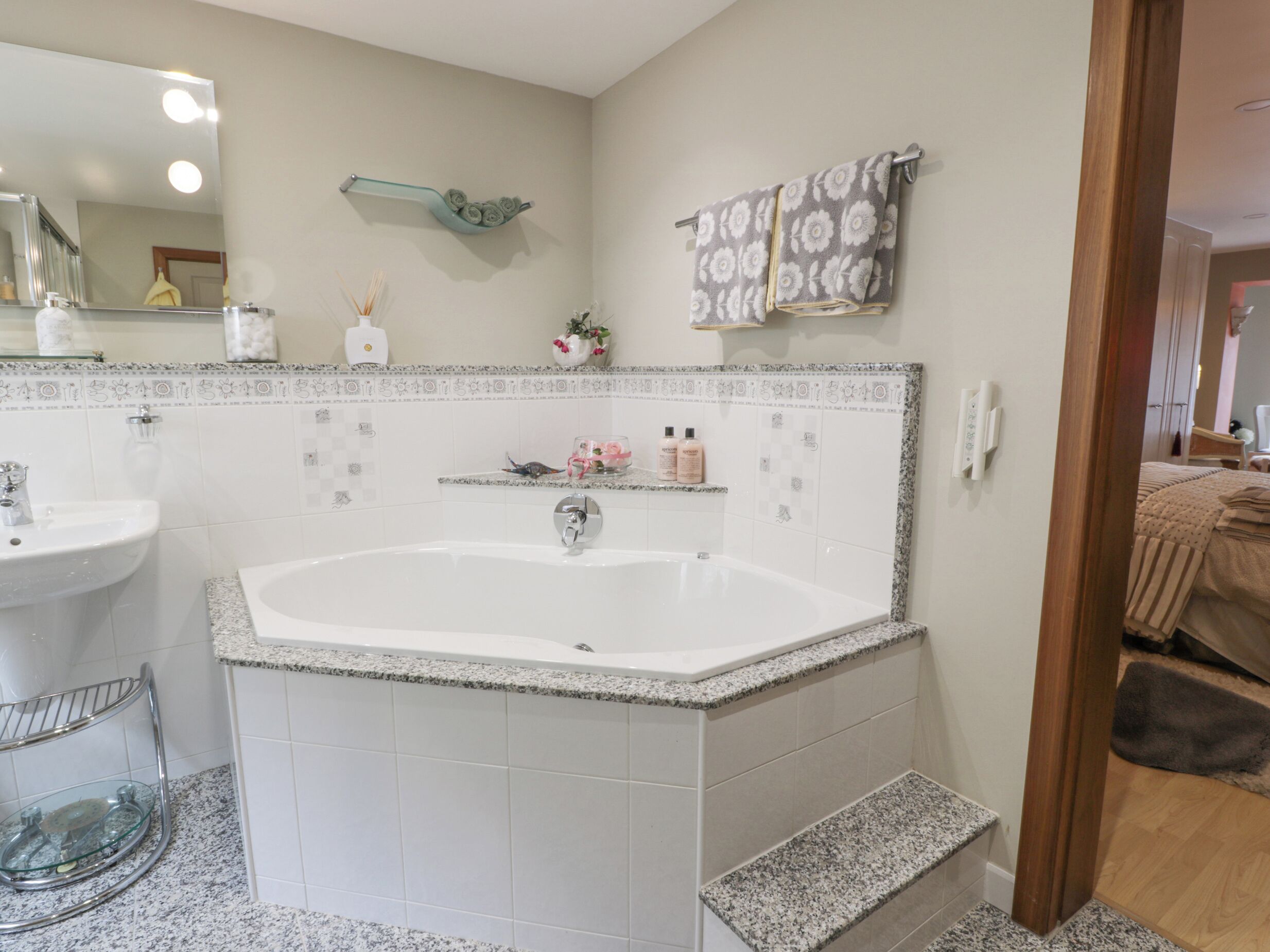 A bathroom with a large bathtub, a sink, a mirror, and a towel rack.