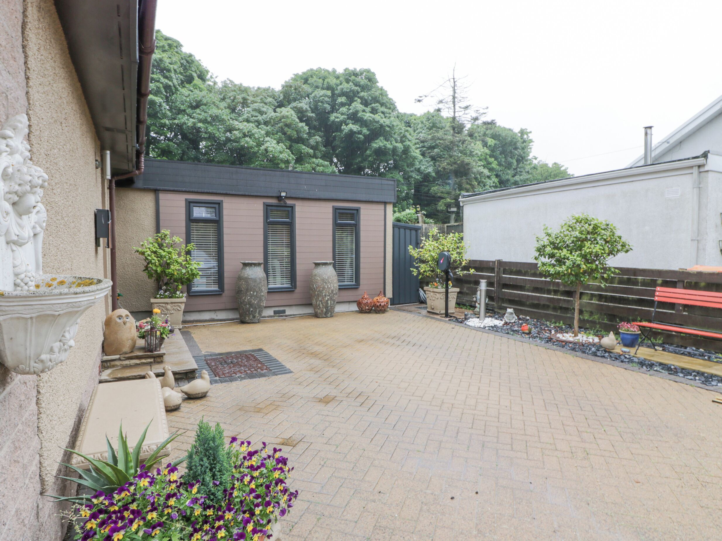 A courtyard with a brick pathway, a small building with shutters, and a bench.
