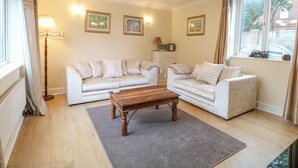 A living room with two sofas, a coffee table, and a chandelier. There are framed pictures on the wall and a window with a view of the outside. - Tiffany's Cottage (Great Yarmouth)